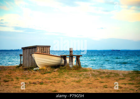 Fischerboot und kleinen Fischen auf dem steinigen Strand bei Sonnenuntergang Licht in Schweden Stockfoto