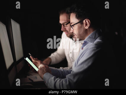 Kollegen mit Smartphones während an einem Schreibtisch sitzen Stockfoto