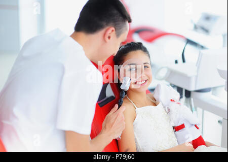 Schönes Lächeln mit weißen Zähnen. Ein Zahnarzt untersucht die Mundhöhle eine junge schöne Mädchen mit einer Lupe in der Zahnarztpraxis. Stockfoto