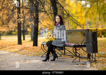 Horizontale Foto, schöne Mädchen sitzen auf der Bank im herbstlichen Park Stockfoto