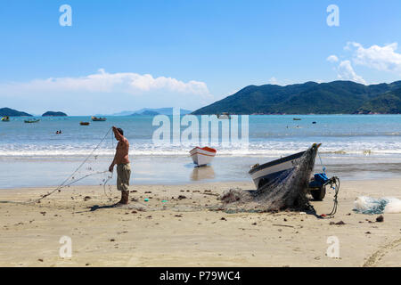 Florianopolis, Santa Catarina, Brasilien. Ein Fischer entwirren sein Netz neben seinem Boot am Strand an einem sonnigen Tag. Stockfoto