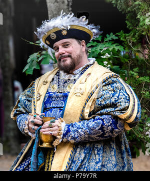 Maryland Renaissance Festival Schauspieler porträtiert König Henry VIII ruht im Freien, bei einem Drink in seinem bejeweled Hände. Er lächelnd vor der Kamera. Stockfoto