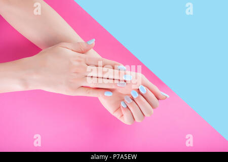 Weibliche hand mit sanft blau Maniküre am Finger Nägel auf Pastell rosa und blauen Hintergrund isoliert. Weiblichkeit und Schönheit Frau Konzept Stockfoto
