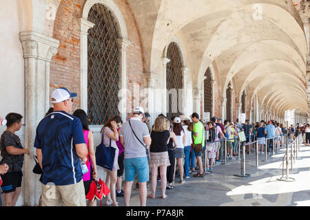 Lange Linie der Touristen Queuing der Dogenpalast oder Palazzo Ducale, Piazza San Marco, Venedig, Venetien, Italien unter der gewölbten Kolonnade außerhalb eingeben. Stockfoto