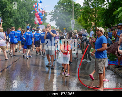 Oak Park, Illinois, USA, 4. Juli 2018. Ein Hausbesitzer auf der Independence Day Parade route kühlt Parade Teilnehmer mit einem Spray von Wasser aus seinem Garten Schlauch in diesem Vorort westlich von Chicago. Temperaturen am 4. Juli wurden weit über 90 °C/32 °C mit einem Index von über 100 ºF. Quelle: Todd Bannor/Alamy leben Nachrichten Stockfoto