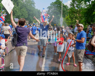 Oak Park, Illinois, USA, 4. Juli 2018. Ein Hausbesitzer auf der Independence Day Parade route kühlt Parade Teilnehmer mit einem Spray von Wasser aus seinem Garten Schlauch in diesem Vorort westlich von Chicago. Temperaturen am 4. Juli wurden weit über 90 °C/32 °C mit einem Index von über 100 ºF. Quelle: Todd Bannor/Alamy leben Nachrichten Stockfoto