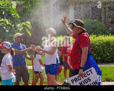 Oak Park, Illinois, USA, 4. Juli 2018. Ein Hausbesitzer auf der Independence Day Parade route kühlt Parade Teilnehmer mit einem Spray von Wasser aus seinem Garten Schlauch in diesem Vorort westlich von Chicago. Temperaturen am 4. Juli wurden weit über 90 °C/32 °C mit einem Index von über 100 ºF. Quelle: Todd Bannor/Alamy leben Nachrichten Stockfoto