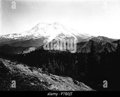 . Englisch: Mount Rainier von Mount Beljica, Washington gesehen, Ca. 1907. Englisch: Hinweis auf negative Hülse: Beljika anzeigen Mann mit Gewehr. Vom Mount Beljica, ein 5,486-ft. Peak eine Meile westlich des Mount Rainier National Park boundary 5 Meilen nordöstlich von Ashford im Südosten Pierce County. Der erste Name war Beljacka Berg- und wurde von einem Pionier der Siedler namens Mesler, die die Initialen der Vornamen seiner Kinder und einige Ihrer Freunde, die sich auf einer Wanderung in den Bergen im Juli 1897 ging verwendet. Themen (LCTGM): Berge - Washington (State) Themen (LCSH): Rainier, Mount (Waschen Stockfoto