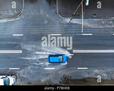 Blaues Auto auf nasser Straße nach starkem Regen. Spritzer und Pfützen auf der Straße überschwemmt. Luftaufnahme Stockfoto