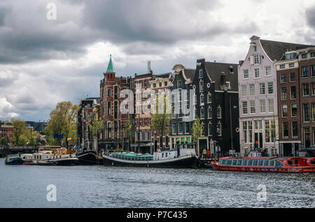 Amsterdam, Niederlande - 27 April 2017: Hausboote und Binnenschiffe, die Binnenamstel canal gegen typische holländische Häuser mit Flagge der Niederlande und Stockfoto