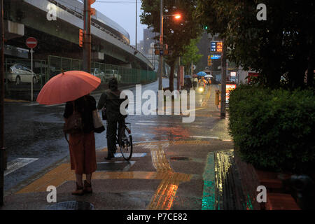 Osaka, Japan - Juli 5, 2018: Frau mit Sonnenschirm und Mann reiten Fahrrad warten, Straße überqueren, bei starkem Regen Stockfoto