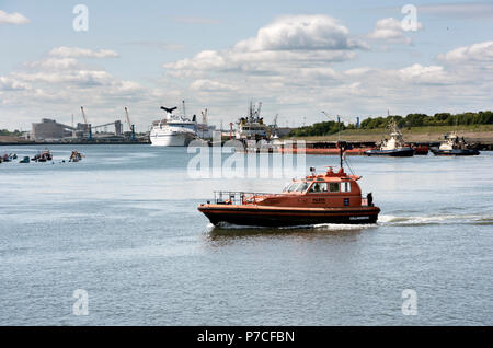 Ein Pilot Boot überquert den Fluss Tyne, mit einem Schiff im Hafen im Hintergrund angedockt, North Shields, Tyneside, Großbritannien Stockfoto