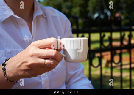 Junge Frau mit einer Tasse Kaffee im Garten an einem sonnigen Sommertag Stockfoto