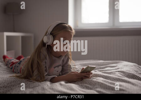 Mädchen hören Musik auf Handy mit Kopfhörer im Schlafzimmer Stockfoto