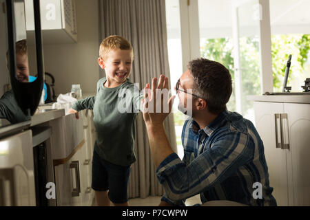 Vater und Sohn geben hohe fünf Miteinander in der Küche Stockfoto