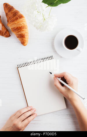 Woman's Hand schreiben im Notebook auf weissem Holztisch. Arbeitsplatz und Konzept, morgen Zeit, Ansicht von oben. Stockfoto