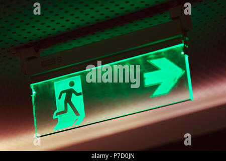 Beleuchtete grüne Notausgang Schild, was darauf hinweist, dass der Fluchtweg ist auf der rechten Seite Stockfoto
