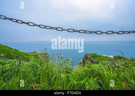 Metall Kette blockiert den Zugriff auf die gefährlichen und steilen Klippen an der Küste von Cornwall auf dem Gipfel des Berges St Michaels in Marazion, Cornwall, England Stockfoto