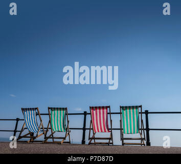 Sidmouth - vier bunten Liegestühle (Liegestühle) auf der Strandpromenade, blauer Himmel über dem Kopf Stockfoto