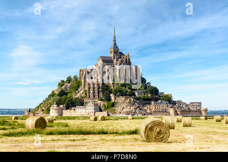 Der Mont Saint-Michel tidal Island in der Normandie, Frankreich, mit runden Strohballen auf einem Feld in den Vordergrund unter einem blauen Himmel mit faserige Wolken. Stockfoto