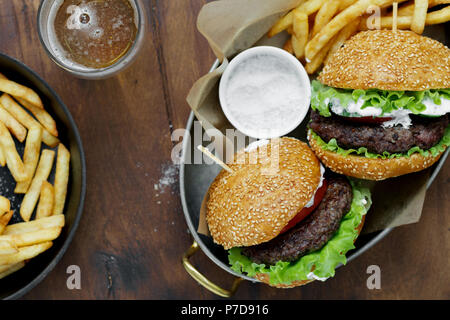 Ansicht von oben Burger, Pommes Frites, Sauce serviert in Pfannen auf Holztisch mit Bier, Ansicht von oben Stockfoto