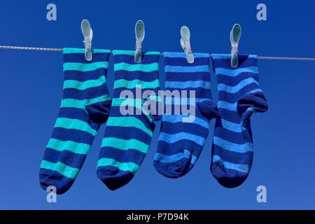 Zwei Paar gestreifte blaue Socken hängen an einer Wäscheleine vor blauem Himmel an einem sonnigen Tag. Stockfoto