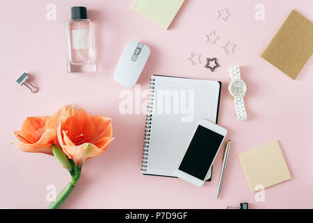 Flach, Ansicht von oben Bürotisch Schreibtisch. Feminine Schreibtisch Arbeitsbereich mit Blumen Amaryllis, Notebooks, Pen, Smartphone, Computer Maus, Frauen Armbanduhr und Stockfoto