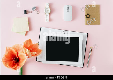 Flach, Ansicht von oben Bürotisch Schreibtisch. Feminine Arbeitsbereich mit Tablet mit leerer Bildschirm, Notebook, Computer Maus, Armbanduhr und Blumen Amaryllis auf Stockfoto