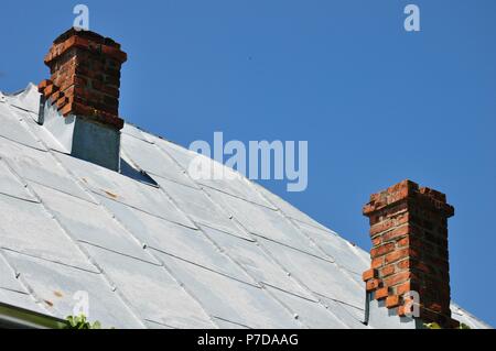 Blatt grau Metall Dach mit zwei traditionellen Schornsteine aus Backstein auf ein Haus auf dem Land, mit einem klaren blauen Himmel Hintergrund Kopie Raum Stockfoto