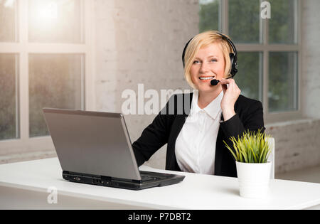 Call Center Betreiber, blonde Frau in schwarzer Jacke und weißem T-Shirt Arbeiten am Laptop über Kopfhörer in Weiß gekleidet Büro Stockfoto