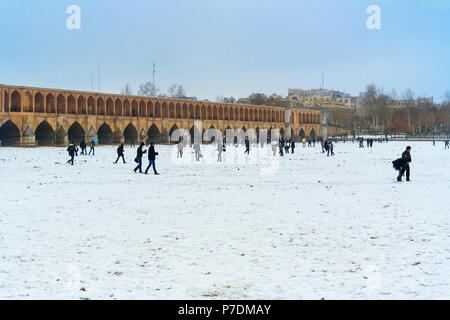 Kinder spielen im Schnee im ausgetrockneten Flussbett des Zayandeh Flusses neben er atemberaubende Khajou Khaju Brücke in Isfahan, Iran. Stockfoto