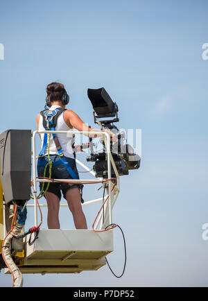 Ansicht der Rückseite des einzigen Fernsehen Kamerafrau auf erhöhten Plattform angehoben hoch in der Luft Dreharbeiten Sport Event für live übertragen. Und blauer Himmel. Stockfoto