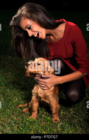 Junge Mädchen in Rot spielt gerne mit Ihrem Hund English Cocker Spaniel lächelnd gekleidet Stockfoto