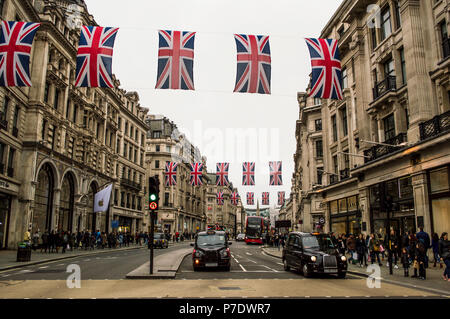 LONDON, UK - April 2018: Die roten Busse und Taxis vorbei unter Union Jack Fahnen vor der königlichen Hochzeit in der Regent Street. Stockfoto