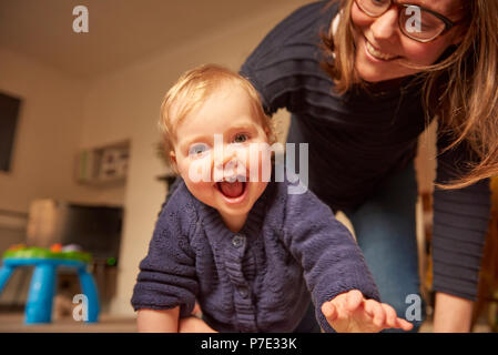 Baby Mädchen mit Mutter krabbeln im Wohnzimmer, Porträt Stockfoto