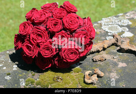 Goldene Hochzeit Ringe stilvoll auf Moss vor der Brautstrauß angeordnet Stockfoto