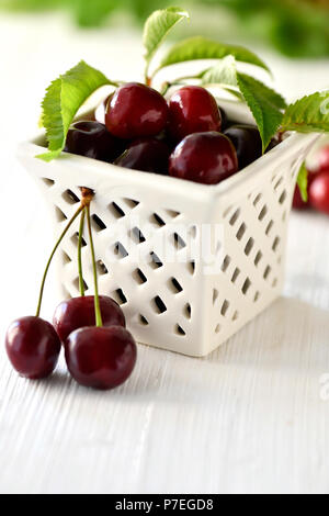 Kirschen in einem Gitter Schüssel auf einem weißen Hintergrund Holz shot mit selektiven Fokus auf Anzeige Text Overlay. Stockfoto