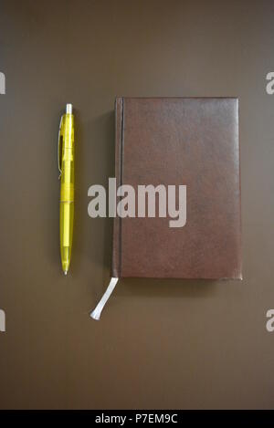 Braun Buch Tagebuch mit einem gelben Stift auf einem Braunen matten Hintergrund. Stockfoto