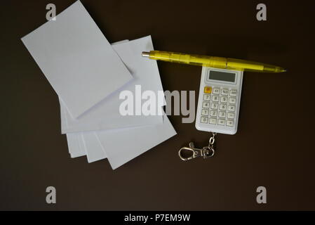 Weiß Taschenrechner mit gelb Kugelschreiber und weißen Blatt Papier auf einem Braunen matten Hintergrund. Stockfoto