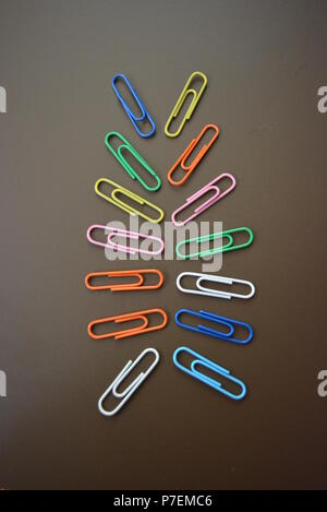 Farbe Klammern in verschiedenen Farben sind verstreut und bunte Clips sind über einen braun matt Hintergrund verbreiten. Stockfoto