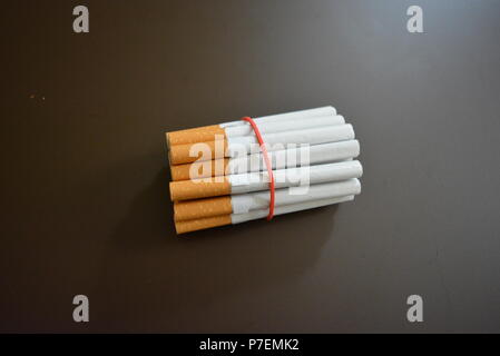 Zigaretten aus der Packung sind mit einem roten Gummi auf einem Braunen matten Hintergrund fixiert. Stockfoto