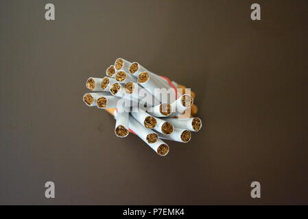 Zigaretten aus der Packung sind mit einem roten Gummi auf einem Braunen matten Hintergrund fixiert. Stockfoto