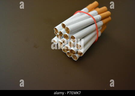 Zigaretten aus der Packung sind mit einem roten Gummi auf einem Braunen matten Hintergrund fixiert. Stockfoto