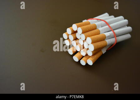 Zigaretten aus der Packung sind mit einem roten Gummi auf einem Braunen matten Hintergrund fixiert. Stockfoto