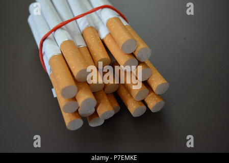 Zigaretten aus der Packung sind mit einem roten Gummi auf einem Braunen matten Hintergrund fixiert. Stockfoto