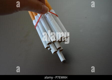 Zigaretten aus der Packung sind mit einem roten Gummi auf einem Braunen matten Hintergrund fixiert. Stockfoto