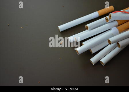 Zigaretten aus der Packung sind mit einem roten Gummi auf einem Braunen matten Hintergrund fixiert. Stockfoto