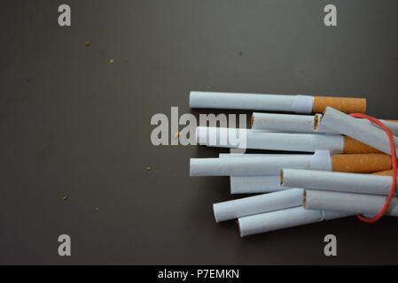 Zigaretten aus der Packung sind mit einem roten Gummi auf einem Braunen matten Hintergrund fixiert. Stockfoto