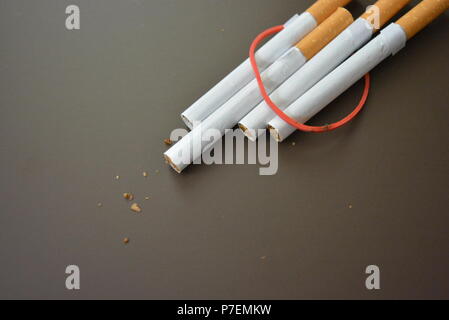 Zigaretten aus der Packung sind mit einem roten Gummi auf einem Braunen matten Hintergrund fixiert. Stockfoto