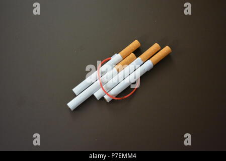 Zigaretten aus der Packung sind mit einem roten Gummi auf einem Braunen matten Hintergrund fixiert. Stockfoto